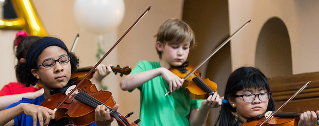 Four young children intently playing the violin